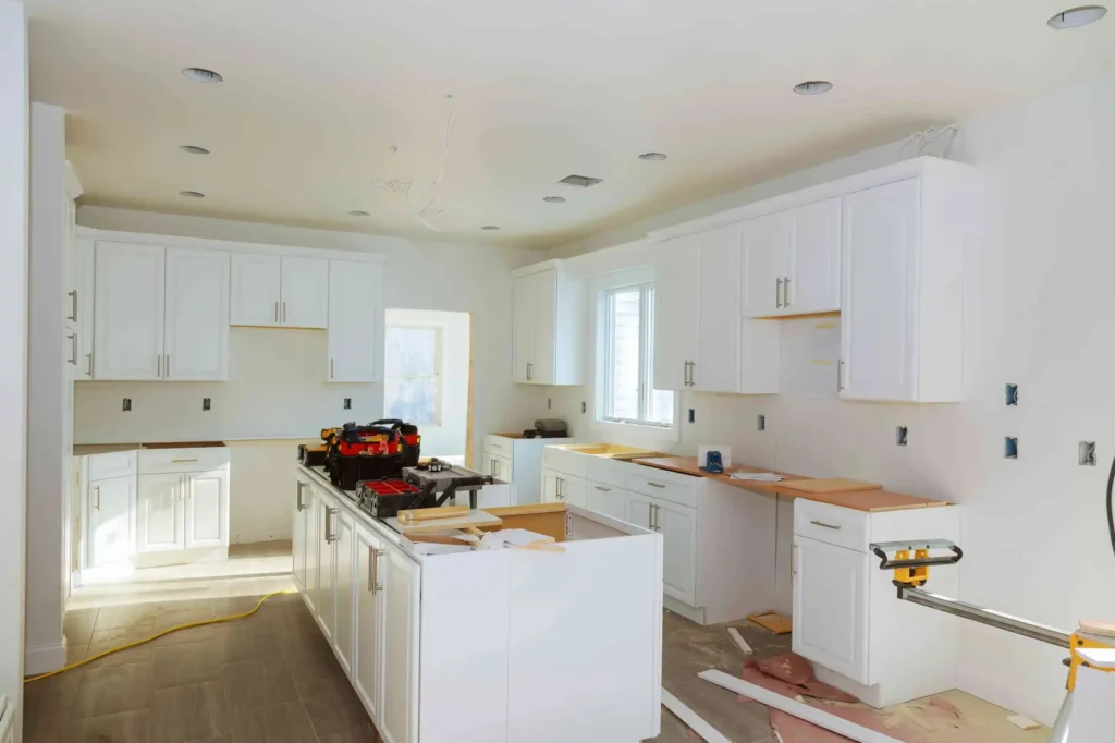 Modern white kitchen under renovation with cabinets and tools installed.